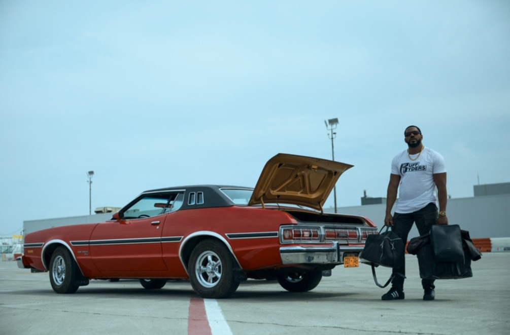 photo of MM from the boys wearing ruff ryders shirt and standing by a car