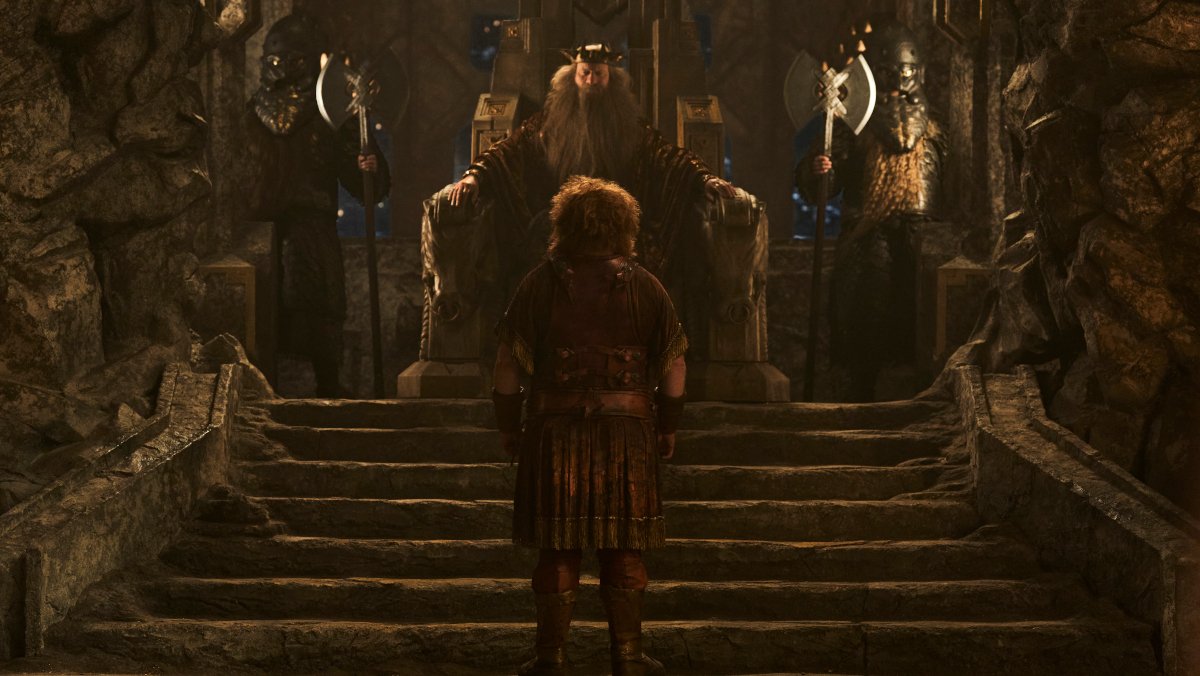 Prince Durin IV stands with his back to the camera in front of his father King Durin III on the throne in The Rings of Power season 2