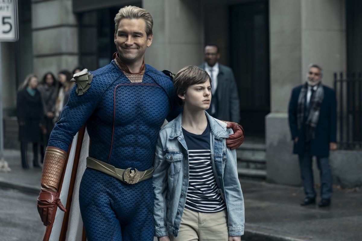 Homelander smiles on the street with his son Ryan beside him