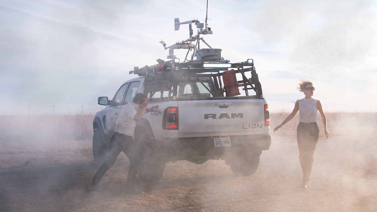 Two people caught in a dust storm near a truck in Twisters